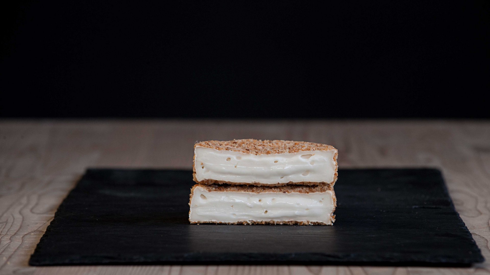 Il caseificio Capriz a Vandoies L'immagine mostra due pezzi di pane croccante o panatura tagliati a metà impilati uno sull'altro, ripieni di formaggio fuso. Il formaggio è morbido, cremoso e si allunga leggermente. L'immagine complessiva dà l'impressione di uno snack di formaggio croccante al forno.