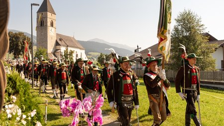 Vacanze sostenibili in Alto Adige Sfilata tradizionale con costumi tipici davanti a una chiesa in un villaggio soleggiato