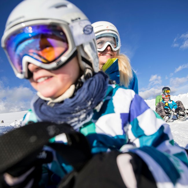 Dove slittare in Alto Adige – Rio Pusteria Bambini e adulti che slittano sulla neve sotto il sole