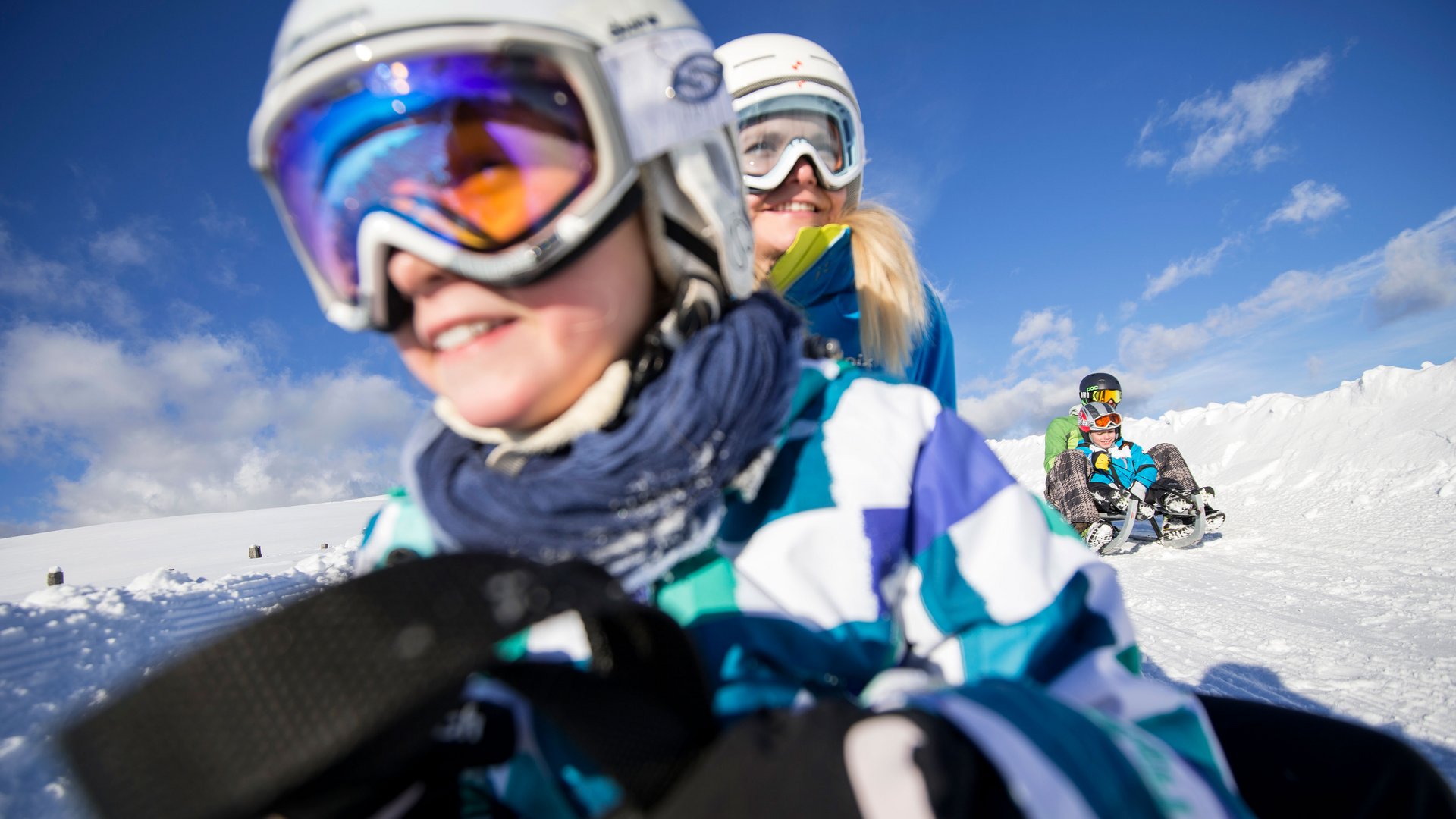 Voglia di slittino? Venite a Terento! Bambini e adulti che slittano sulla neve sotto il sole