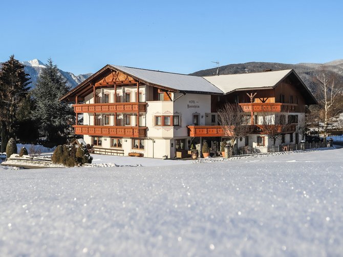 Benvenuti nell’Area Vacanze Sci e Malghe Rio Pusteria! Hotel nella neve con montagne sullo sfondo e cielo sereno