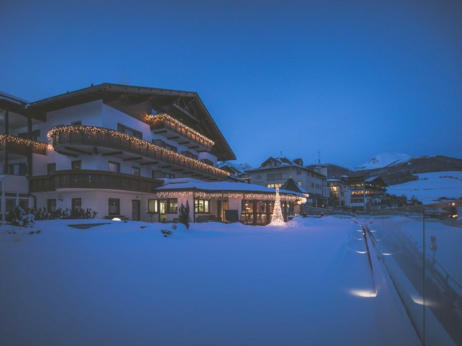 Benvenuti nell’Area Vacanze Sci e Malghe Rio Pusteria! Casa imbiancata con luci di Natale al crepuscolo in montagna