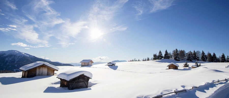 Le località dell’area vacanze Rio Pusteria Baite di legno innevate su montagna soleggiata con cielo azzurro