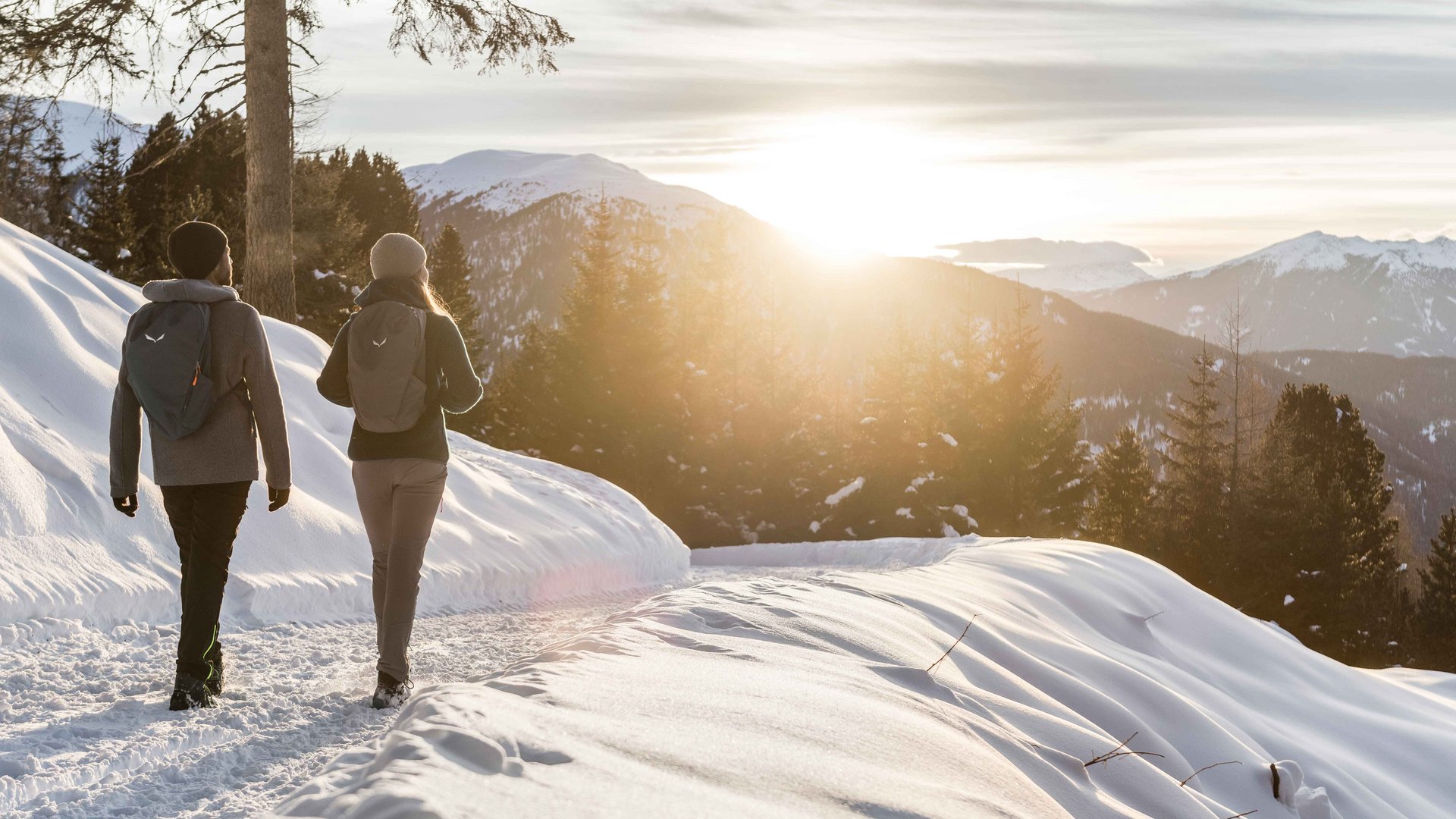 Rio Pusteria: escursioni invernali a Maranza e dintorni Due persone camminano su un sentiero di montagna innevato al tramonto