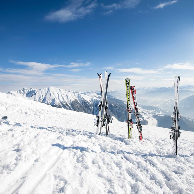 Vacanze sostenibili in Alto Adige Più sci piantati nella neve con montagne innevate e cielo blu sullo sfondo