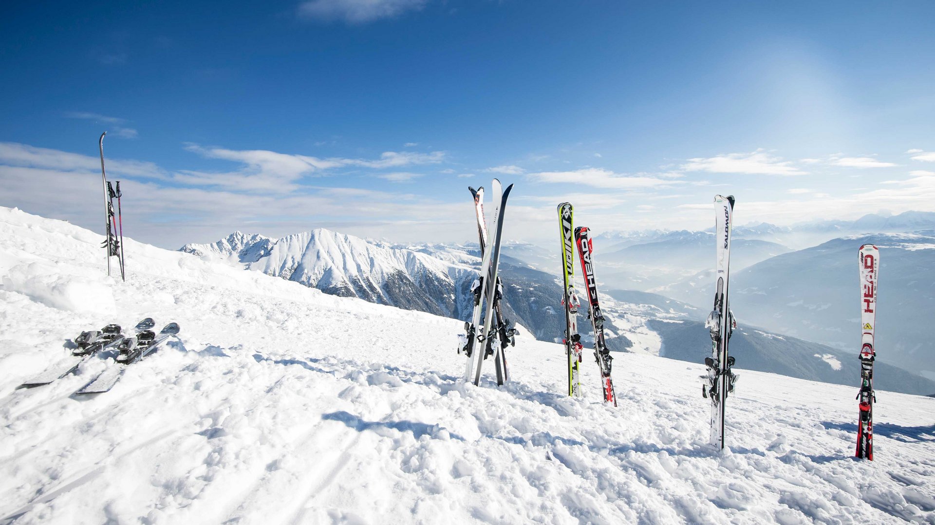 Settimane bianche in Alto Adige Più sci piantati nella neve con montagne innevate e cielo blu sullo sfondo