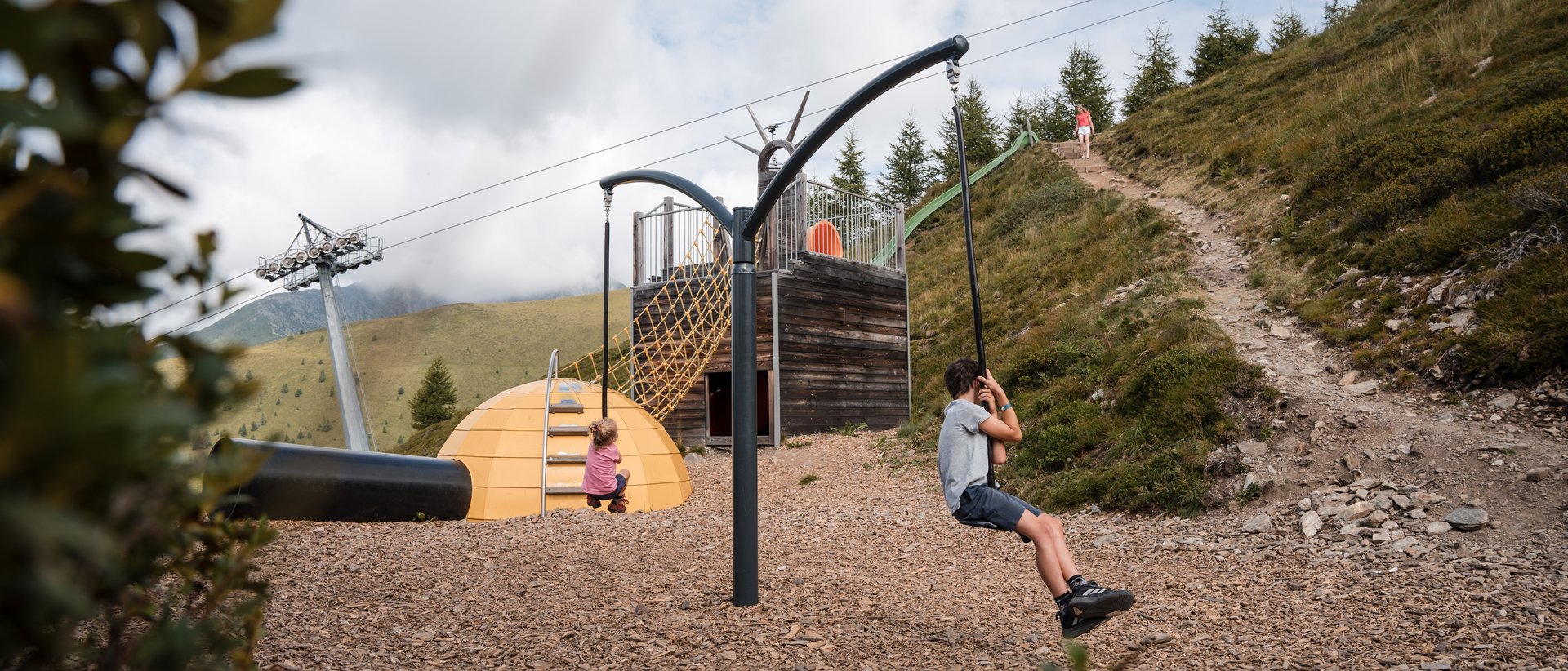 Vacanze in famiglia in Val Pusteria Bambini che giocano su scivolo a fune in parco giochi di montagna