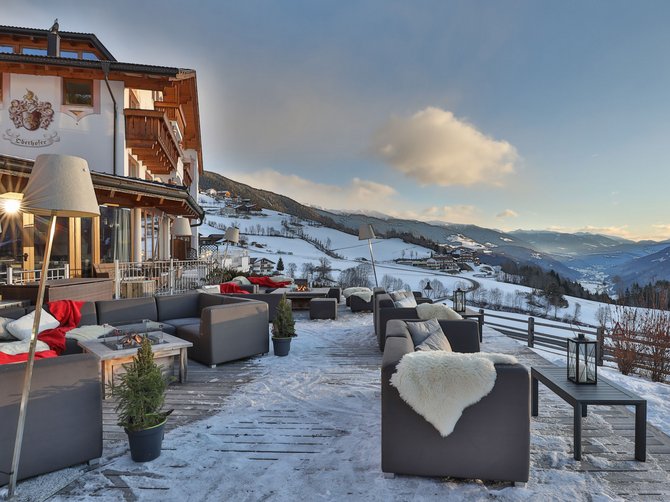 Benvenuti nell’Area Vacanze Sci e Malghe Rio Pusteria! Terrazza con divani e vista sulle montagne con neve e tramonto
