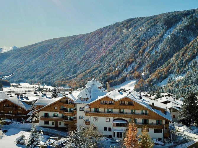 Benvenuti nell’Area Vacanze Sci e Malghe Rio Pusteria! Rifugio coperto di neve davanti a montagna boscosa soleggiata