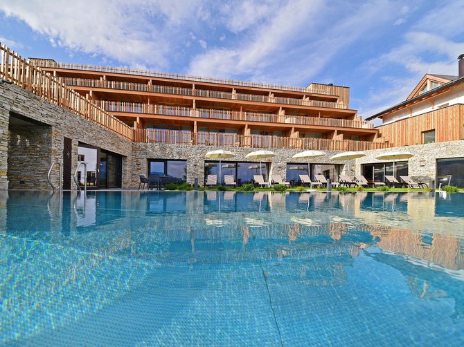 Benvenuti nell’Area Vacanze Sci e Malghe Rio Pusteria! Piscina di un hotel moderno con sdraio e facciata in legno sotto il sole