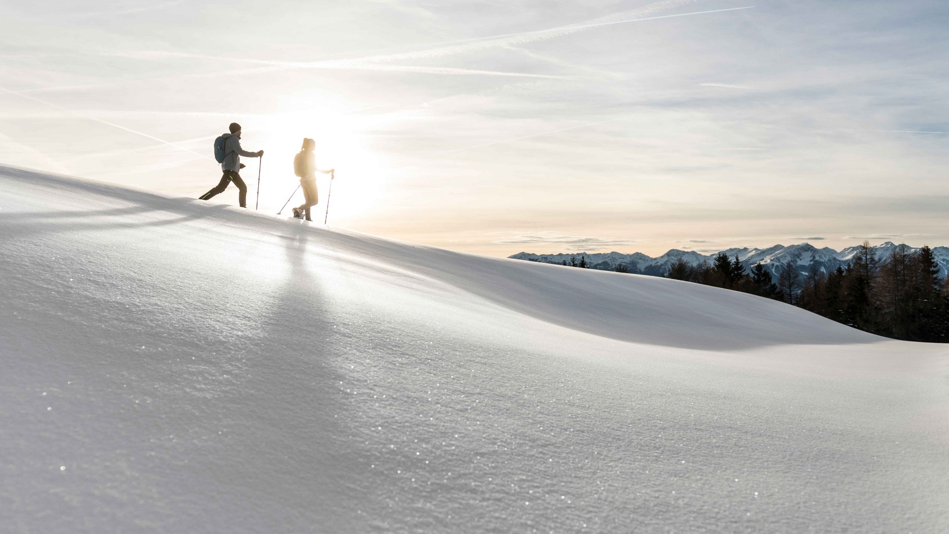 Rio Pusteria: escursioni invernali a Maranza e dintorni Due persone con bastoncini da trekking camminano sulla neve al sole