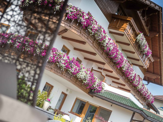 Benvenuti nell’Area Vacanze Sci e Malghe Rio Pusteria! Balconi di una casa con fiori bianchi e rosa in fioriere