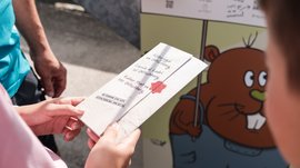 Outdoor Escape sul Monte Gitschberg Persona tiene volantino per caccia ai ladri sul Gitschenberg davanti a tabellone colorato