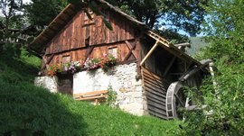 Il Sentiero dei Mulini a Terento Vecchia casa in legno con ruota ad acqua e fiori sul davanzale in paesaggio verde