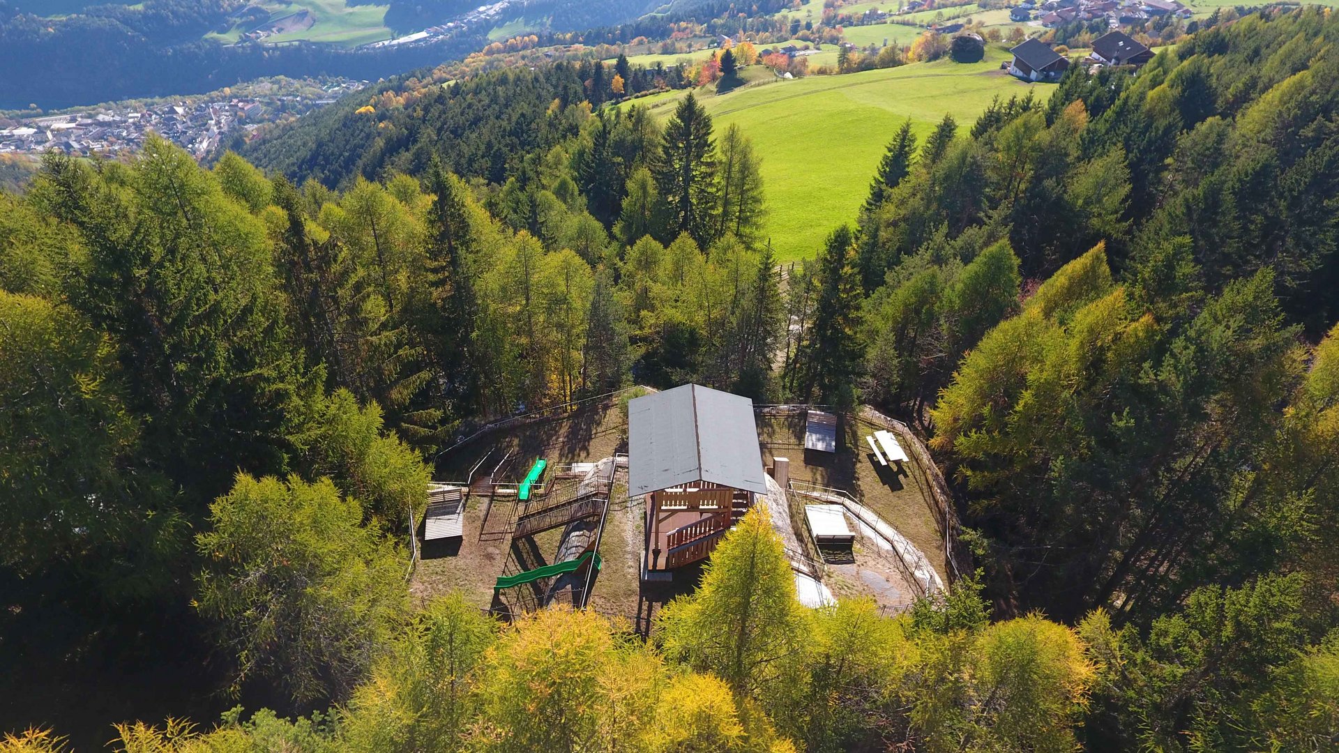 La zona ricreativa bunker di Spinga L'immagine mostra un paesaggio boschivo con un piccolo edificio al centro, circondato da alberi. Sullo sfondo si estendono colline e valli verdi, in cui sono visibili sparsi case e campi.