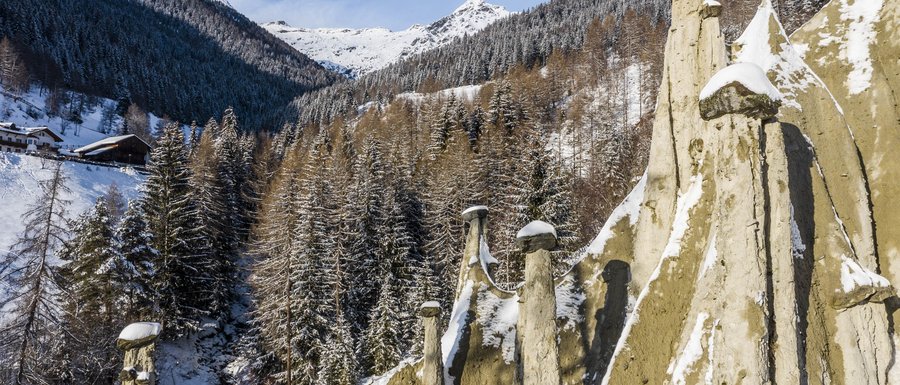 Le località dell’area vacanze Rio Pusteria Piramidi di terra innevate con bosco e montagne sullo sfondo