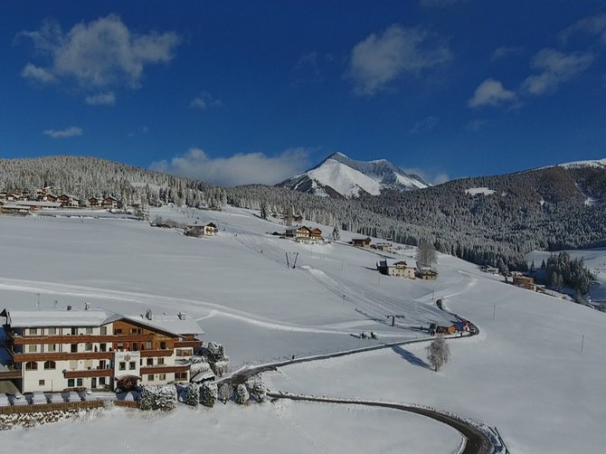Benvenuti nell’Area Vacanze Sci e Malghe Rio Pusteria! Paesaggio invernale con hotel innevato e montagne sotto cielo sereno