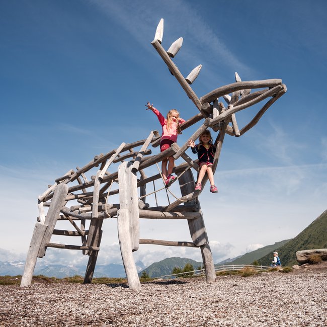 Vacanze in famiglia in Val Pusteria Due bambini giocano su una grande renna di legno in un parco giochi soleggiato