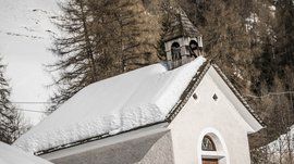 Quando si dice idilliaco… ecco a voi Fundres L'immagine mostra una piccola cappella bianca come la neve con un tetto coperto di neve. Il campanile in legno si trova sul tetto e sullo sfondo si vedono alberi e pendii coperti di neve.