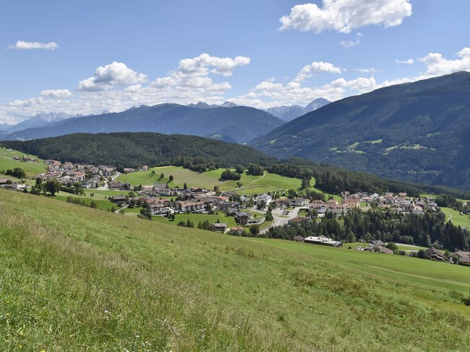 Le località dell’area vacanze Rio Pusteria Vista di un villaggio in una valle verde con montagne e cielo azzurro