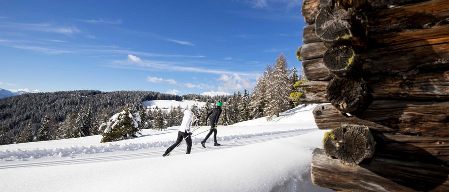 Le località dell’area vacanze Rio Pusteria Due sciatori di fondo su pista innevata accanto a una baita di legno