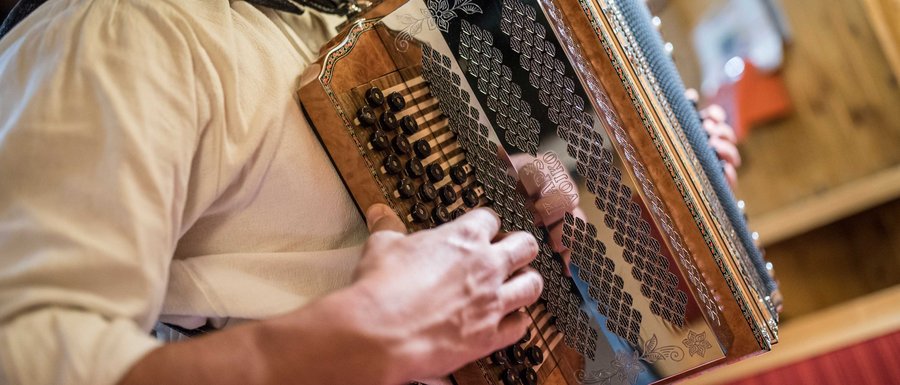 Le località dell’area vacanze Rio Pusteria L'immagine mostra una persona che suona una fisarmonica tradizionale. L'attenzione è sulle mani che azionano i pulsanti e i tasti dello strumento, mentre la fisarmonica presenta dettagliate decorazioni.