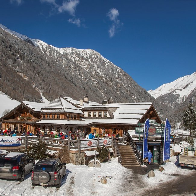 Restaurant Pizzeria Die Mühle Edificio in legno in paesaggio innevato alpino con auto parcheggiate e attrezzature da sci