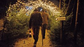 L’Avvento di Terento Due uomini con bastone e lanterna camminano in sentiero boschivo illuminato alla neve