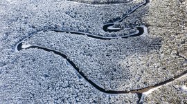 La frazione montana di Spinga L'immagine mostra un paesaggio innevato visto dall'alto, in cui un fiume stretto e tortuoso serpeggia attraverso una fitta foresta coperta di neve. Il fiume si distingue scuro dagli alberi bianchi, creando forti contrasti.