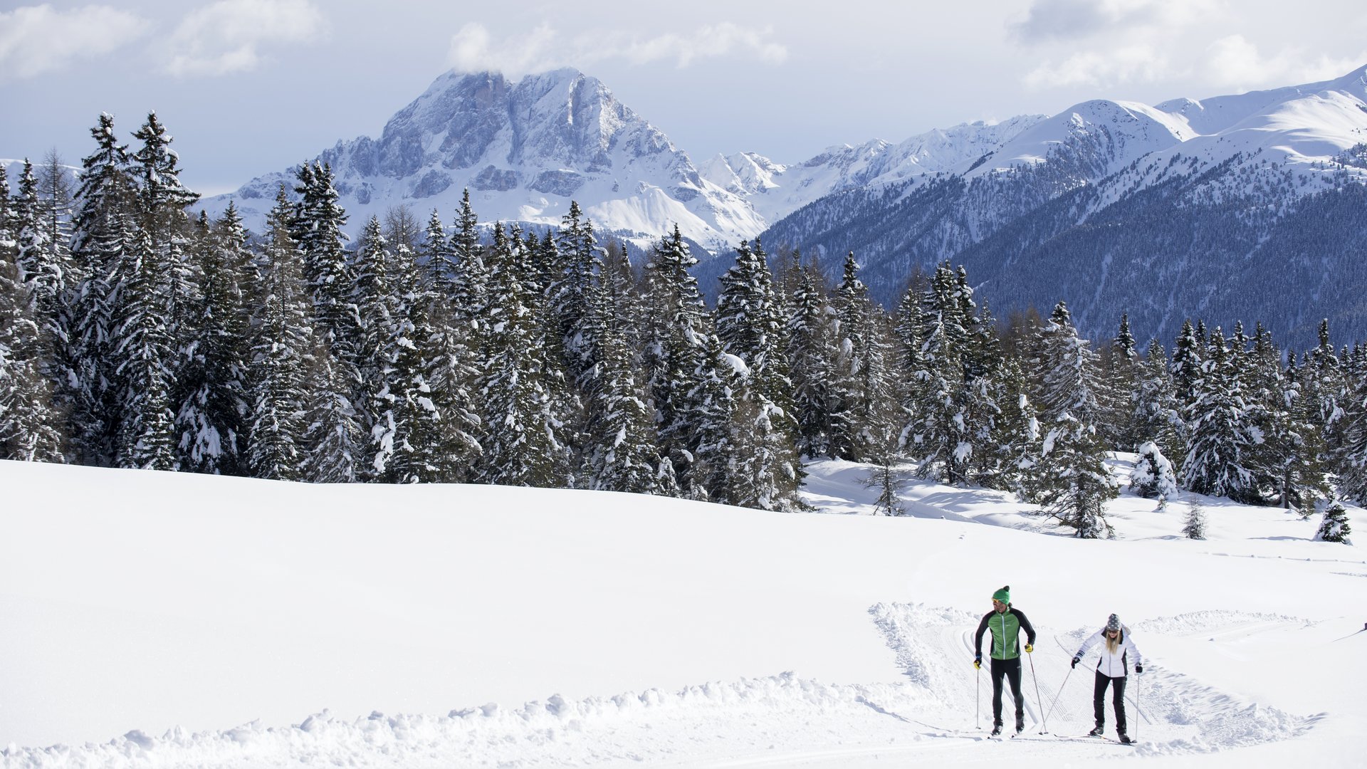 La pista di fondo sull’Alpe di Rodengo e Luson Due sciatori di fondo su percorso innevato con montagne e bosco sullo sfondo