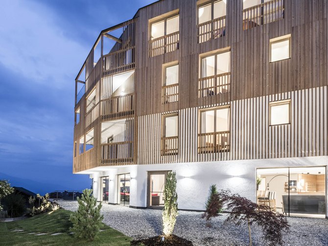 Benvenuti nell’Area Vacanze Sci e Malghe Rio Pusteria! Casa moderna in legno con grandi finestre al crepuscolo