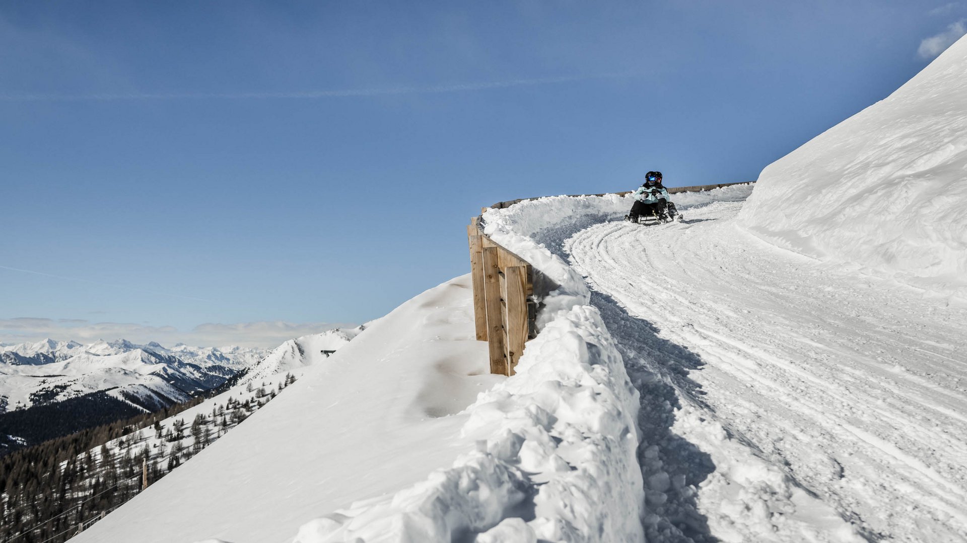 Dove slittare in Alto Adige – Rio Pusteria Persona che slitta su una pista innevata in montagna con cielo blu