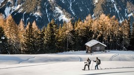 L’Alpe di Rodengo e Luson Due persone camminano nella neve davanti a una baita e alberi di conifere