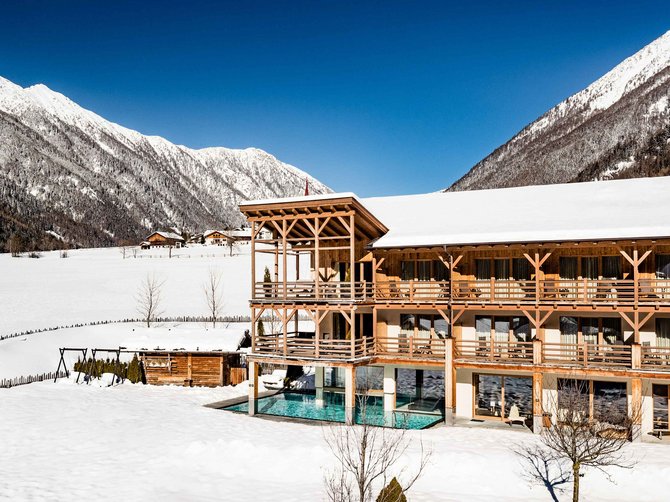 Benvenuti nell’Area Vacanze Sci e Malghe Rio Pusteria! Hotel con piscina esterna nella neve tra le montagne sotto cielo azzurro