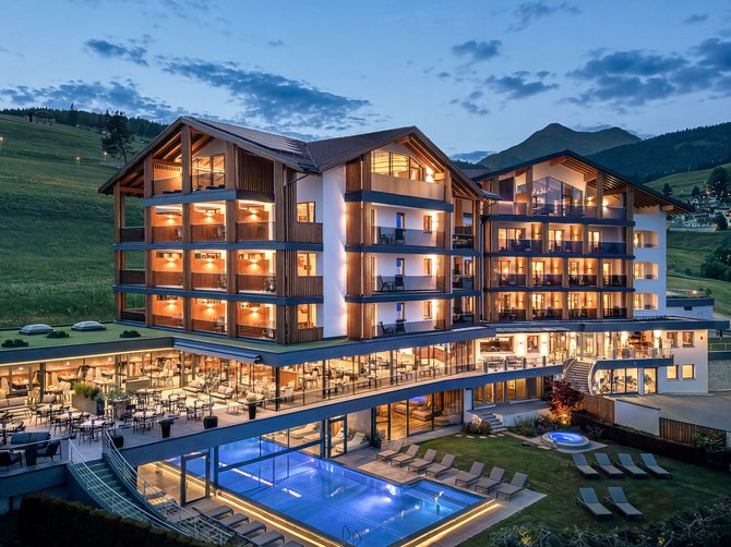Benvenuti nell’Area Vacanze Sci e Malghe Rio Pusteria! Hotel illuminato con piscina esterna e lettini in montagna al crepuscolo