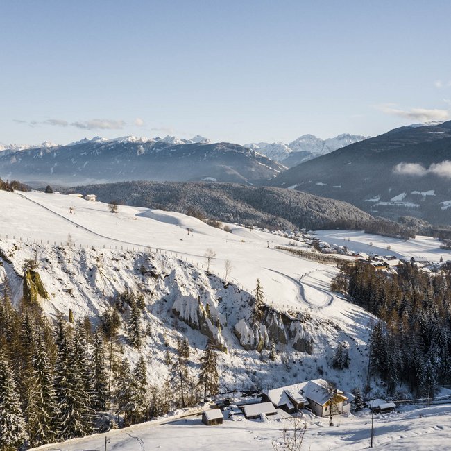 Dove slittare in Alto Adige – Rio Pusteria Paesaggio alpino innevato con case e foresta sotto un cielo sereno