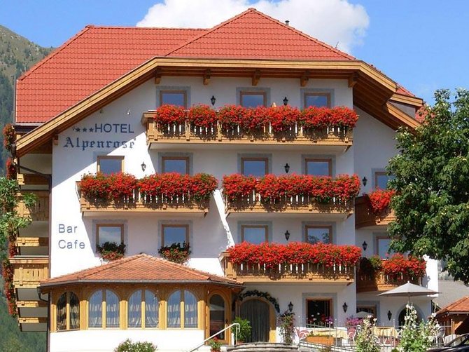 Benvenuti nell’Area Vacanze Sci e Malghe Rio Pusteria! Hotel alpino con fiori rossi sui balconi davanti alle montagne