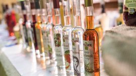 Shopping a Rio di Pusteria (BZ) L'immagine mostra una fila di bottiglie con vari liquori, disposte fianco a fianco. Ogni bottiglia ha un'etichetta con motivi e testi diversi che indicano sapori o ingredienti differenti.