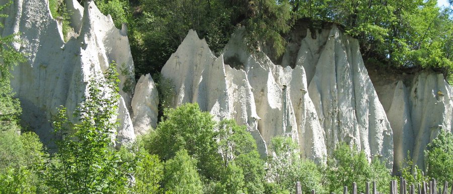 Le località dell’area vacanze Rio Pusteria Formazioni rocciose con recinzione di pali di legno e alberi verdi al sole