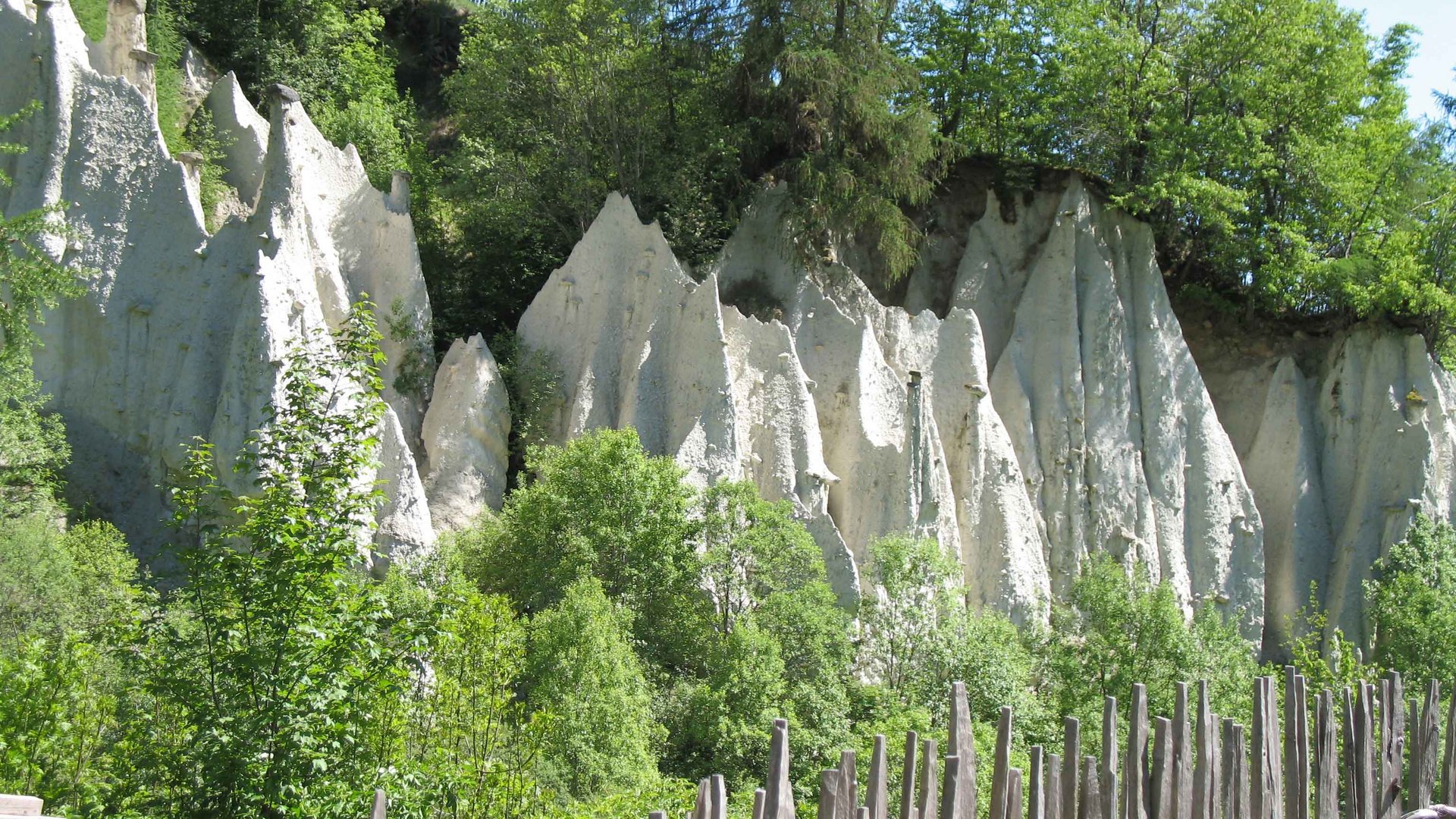 Le piramidi di terra di Terento Formazioni rocciose con recinzione di pali di legno e alberi verdi al sole