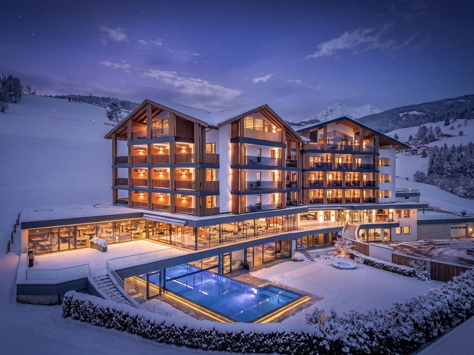 Benvenuti nell’Area Vacanze Sci e Malghe Rio Pusteria! Hotel illuminato con piscina esterna in paesaggio montano innevato di notte
