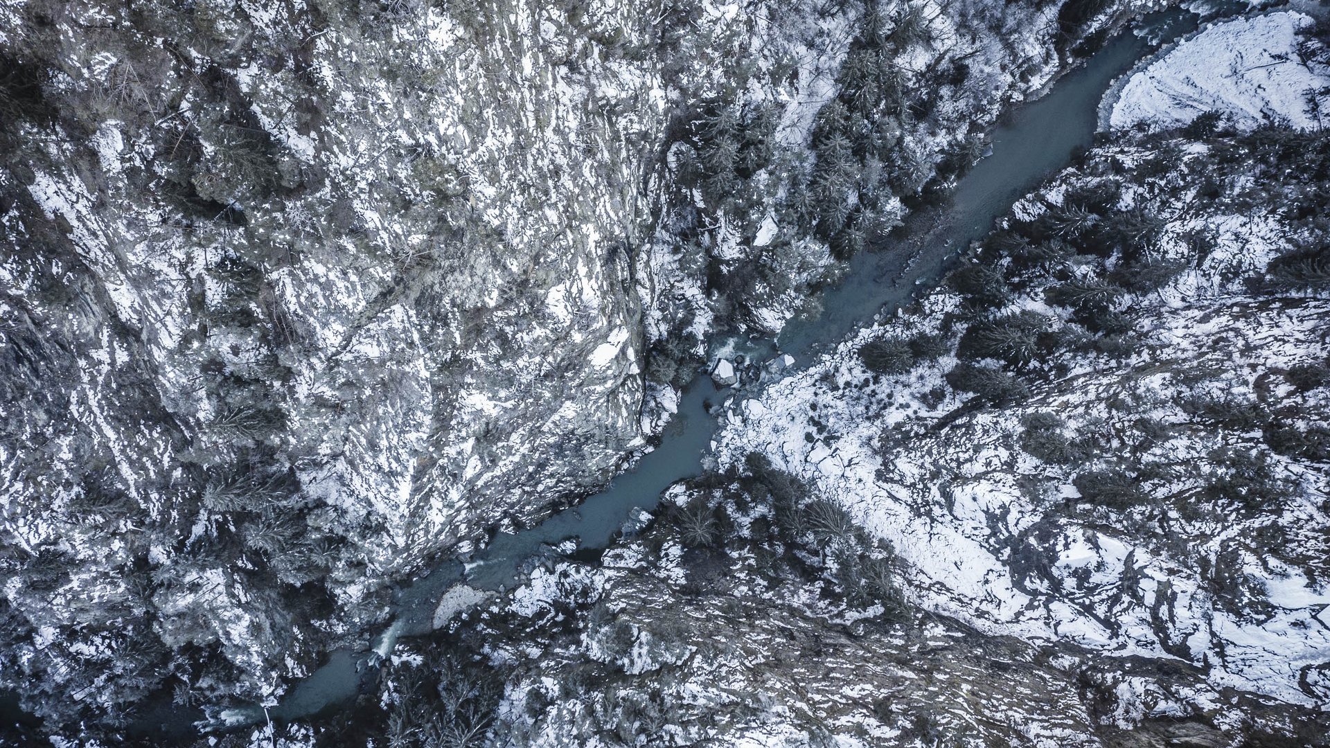 Il paradiso escursionistico di Rodengo L'immagine mostra una vista aerea di una profonda gola attraverso la quale scorre un fiume tortuoso. Le pareti rocciose ripide, coperte di neve, e gli alberi scuri e spogli lungo la gola rafforzano l'impressione di una natura selvaggia, aspra e invernale.