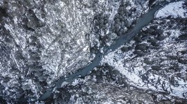Il paradiso escursionistico di Rodengo L'immagine mostra una vista aerea di una profonda gola attraverso la quale scorre un fiume tortuoso. Le pareti rocciose ripide, coperte di neve, e gli alberi scuri e spogli lungo la gola rafforzano l'impressione di una natura selvaggia, aspra e invernale.