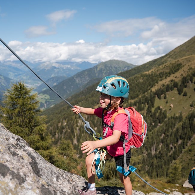 Vacanze in famiglia in Val Pusteria Bambino con casco arrampica una roccia in montagna con imbracatura